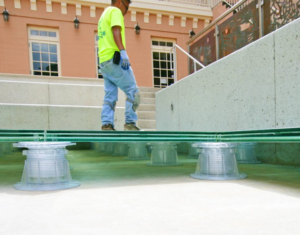 Side View of Glass Pavers Over Pedestals with Worker