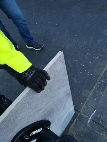 Installer holding kerf-cut porcelain paver with slot visible in corner.