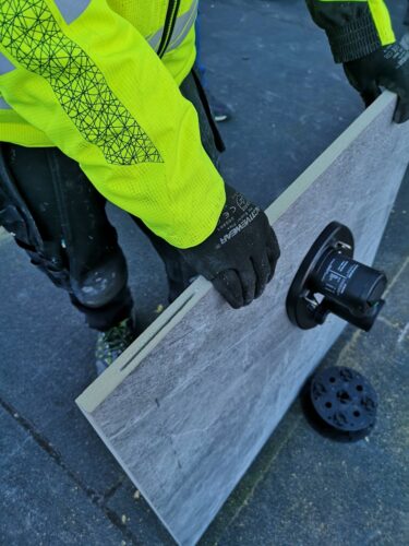 Installer holding kerf-cut porcelain paver with vacuum lifter.